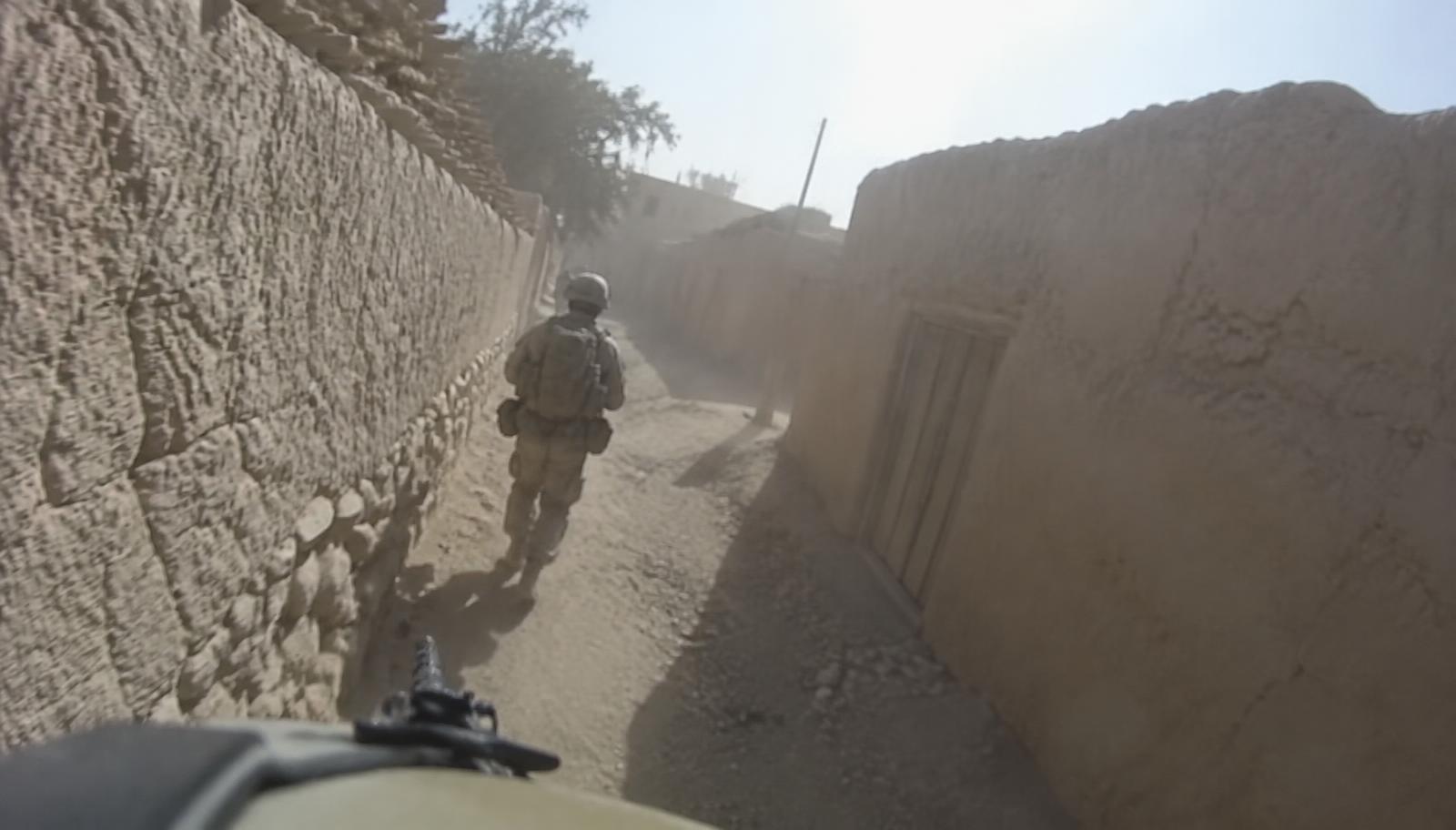 Degraded helmet camera view down a narrow mud-walled alley